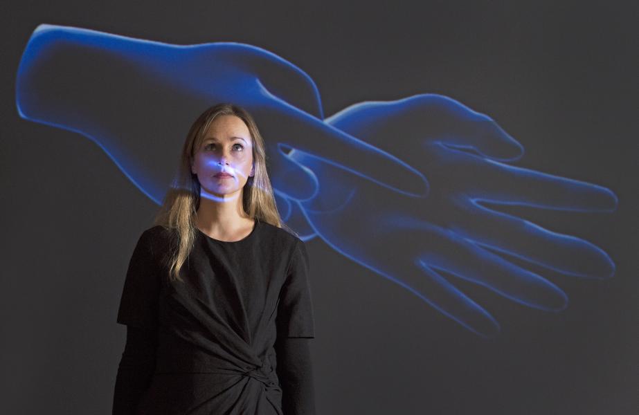 Caroline Grewar, manager of the University of Edinburgh’s Talbot Rice Gallery, stands before artist Marjolijn Dijkman’s projection of two virtual hands.