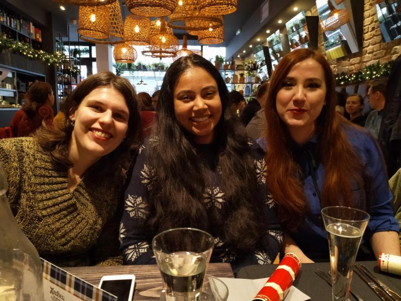 Three lab group members pose for a photo, sitting at a table in a busy restaurant