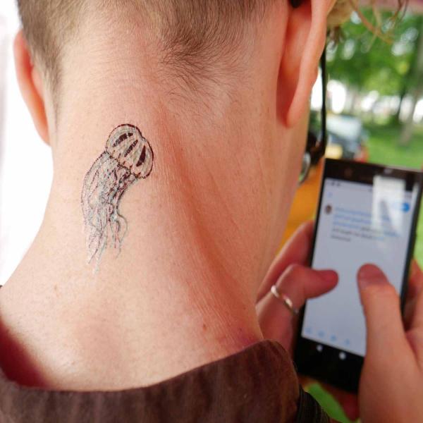 Image of back of a person holding a phone, thier neck has a temporary jellyfish tattoo. 