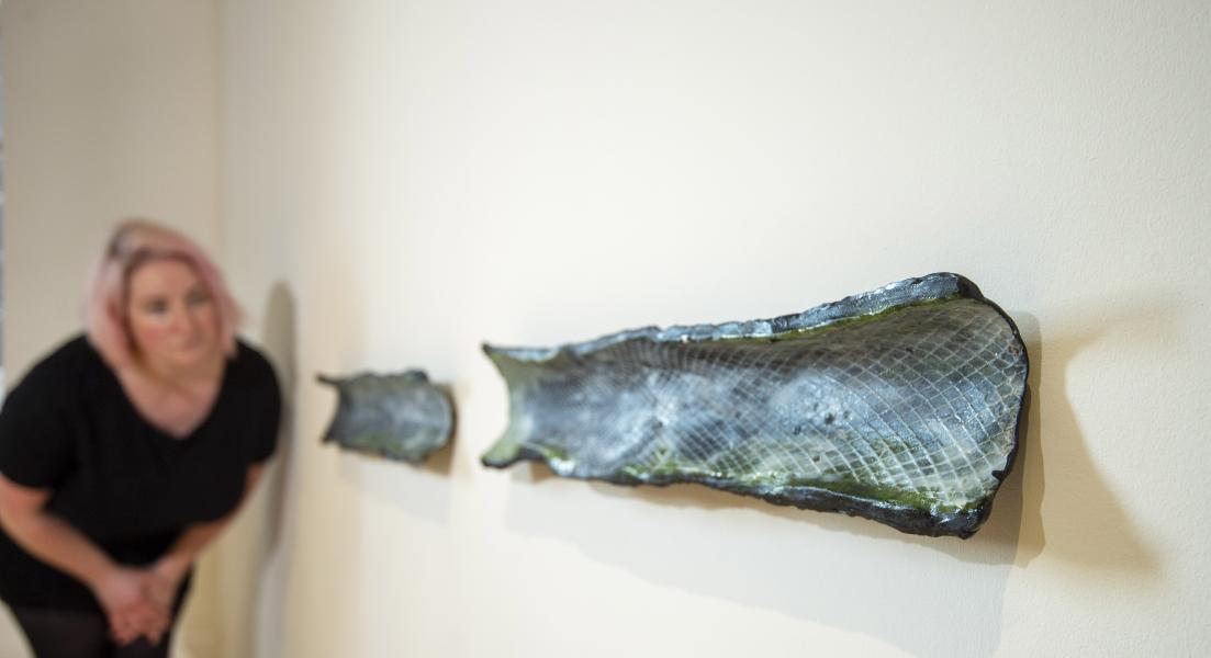 A person looks at two sculptures on a wall by artist Sarah Rose