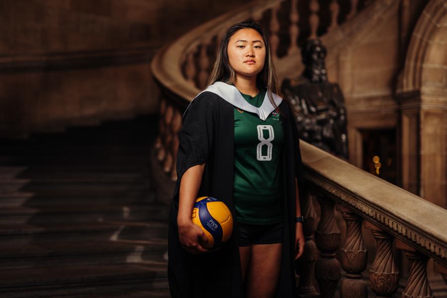 Samantha Lim wearing graduate gown and sports kit holding volleyball on McEwan Hall staircase
