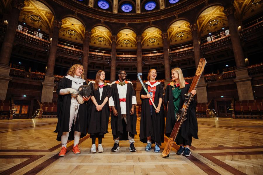 Image of 5 students standing in McEwan Hall in Graduation gowns with university sport kit underneath and equipment