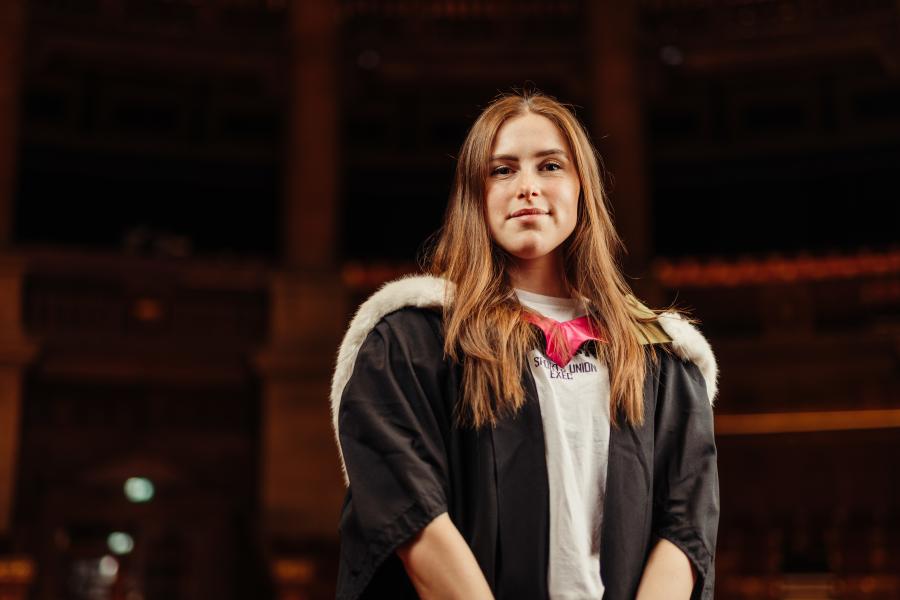 Hannah Campbell wearing graduate gown and sports kit in McEwan Hall 