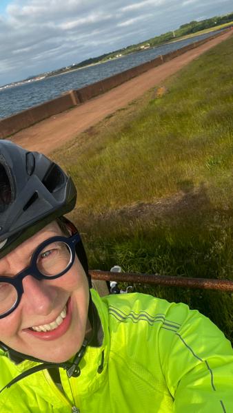A smiling cyclist with a coastal cycle path in the background